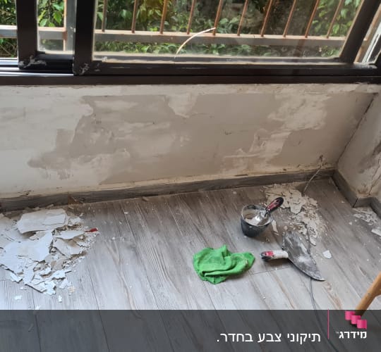 קיר מתוקן עם שפכטל, מברשת ובד ירוק על הרצפה